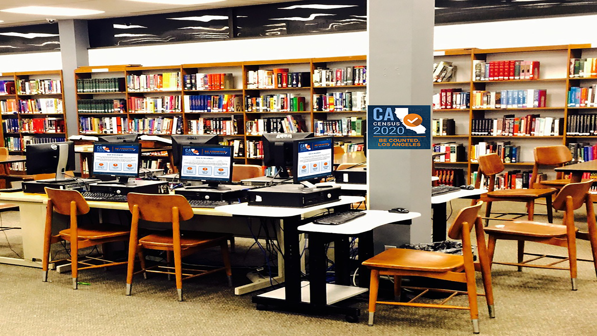 Banner of a library setting with multiple desktop computers displaying images of California Map Logo with text Census 2020 Be Counted Los Angeles.